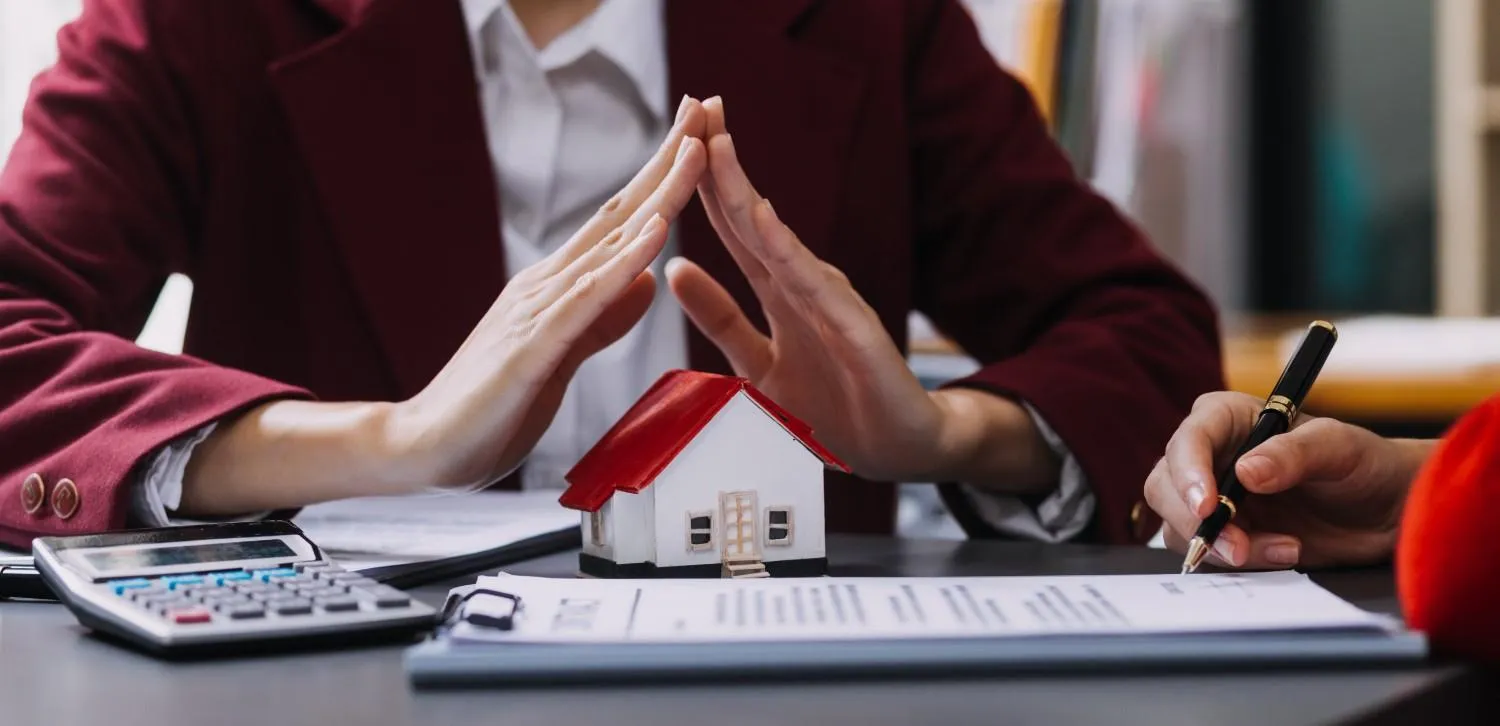 Model house resting on a home policy document beside a calculator